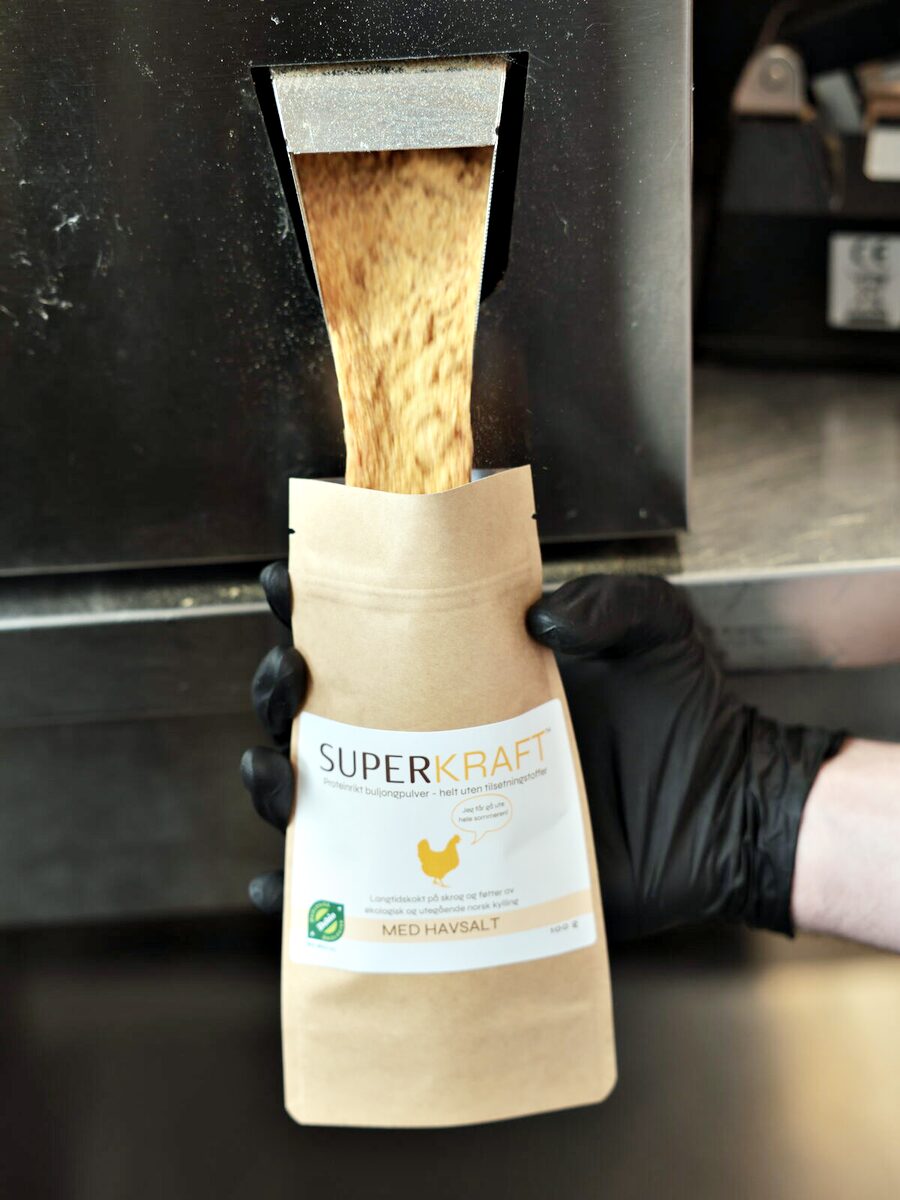 Kraftpulver renner fra fyllemaskinen ned i en pose Superkraft med havsalt, holdt med svarte hansker